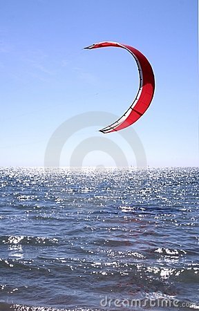 Red Kite Surfer Sail against a blue sky hanging just above the surf.