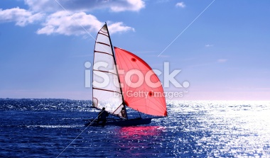 Red Sail, dinghy sailing into the sun on a blue sea